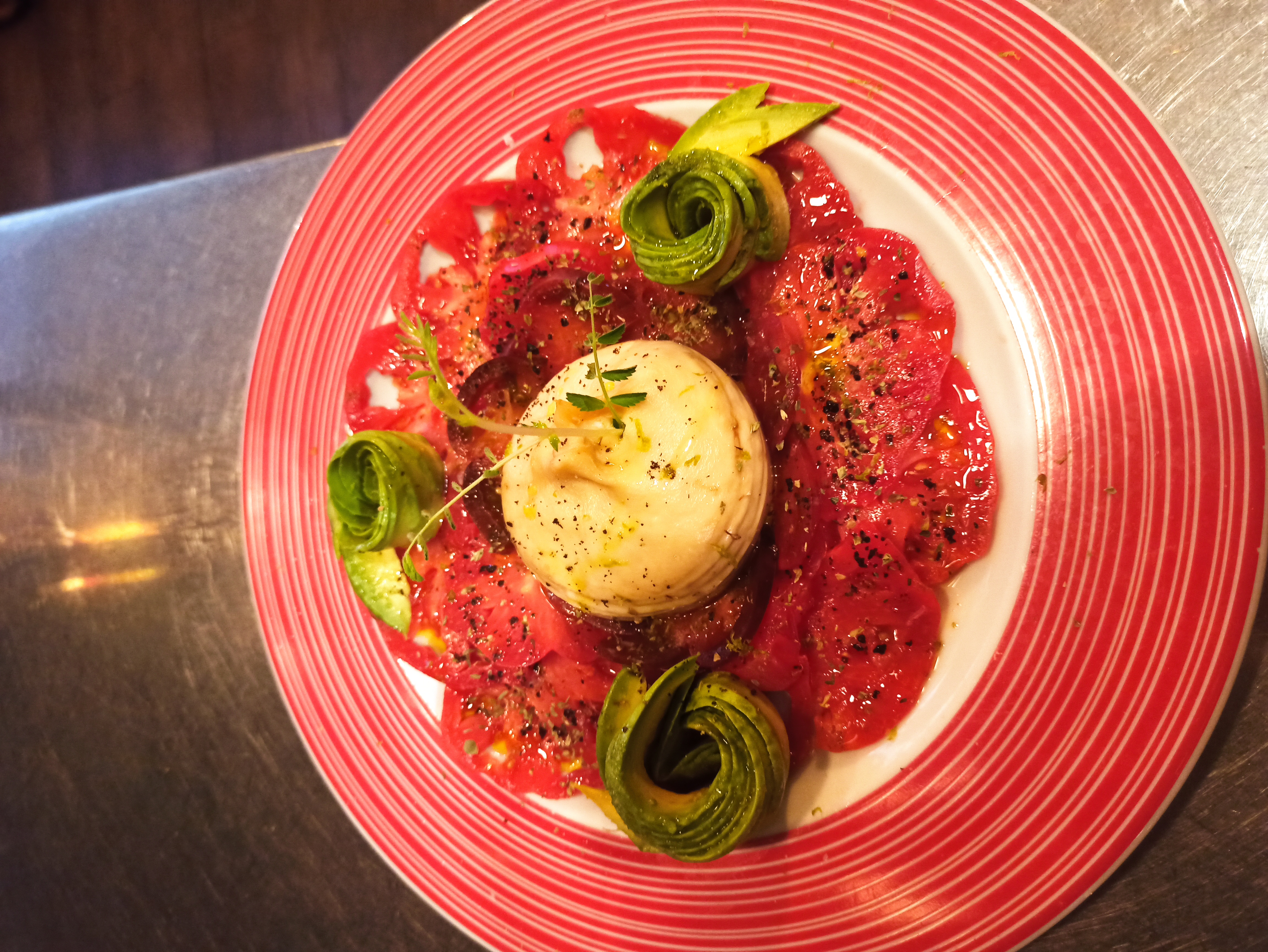 Tomate de temporada con burrata y rosas de aguacate, plato de la carta servido con luz natural